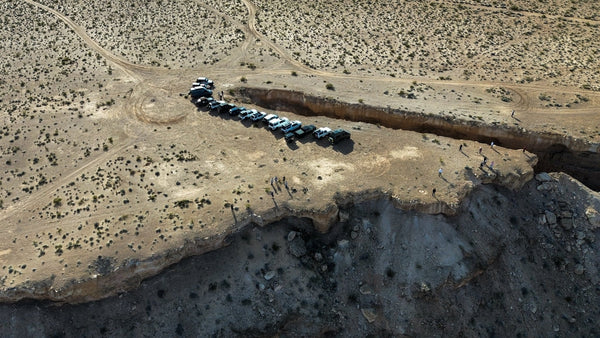 Drone photo showing a line of off-road vehicles parked along the edge of the Double Negative land art site in Nevada, with people exploring the cliffs during the May 23–25, 2026 Weekend Offroad event.