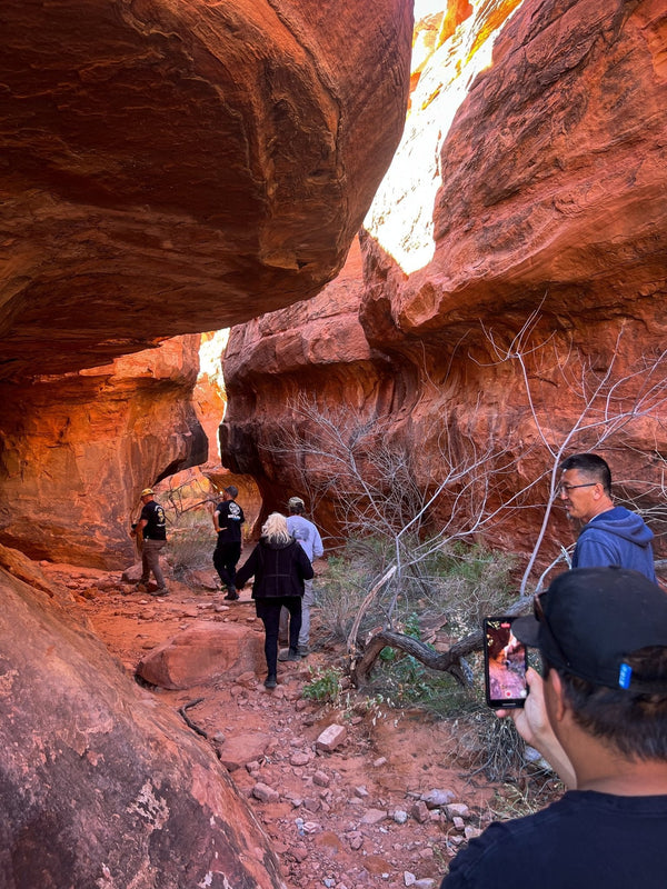 Group of people hiking through a narrow red rock slot canyon during the Weekend Offroad Double Negative adventure, surrounded by colorful sandstone walls and rugged desert terrain.
