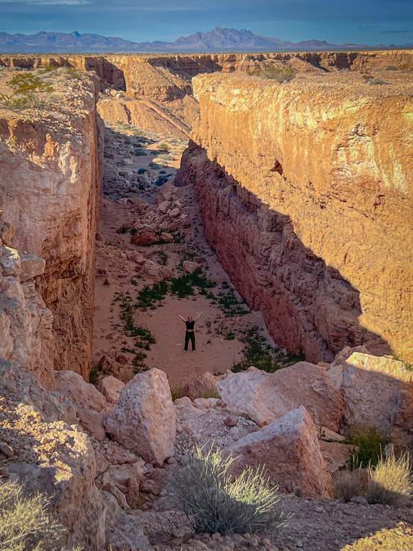 Person standing with arms raised at the bottom of the massive Double Negative land art excavation in the Mojave Desert during a Weekend Offroad overlanding adventure, surrounded by steep sandstone walls and desert landscape.