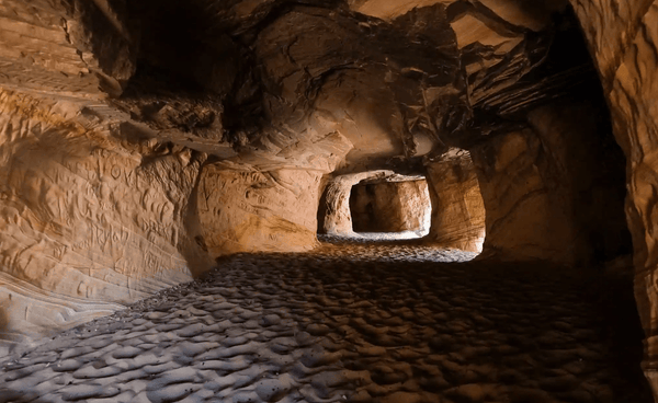 Sandstone tunnel with carved walls and sandy ground explored during the Lake and Canyon Relaxation 2026 trip.