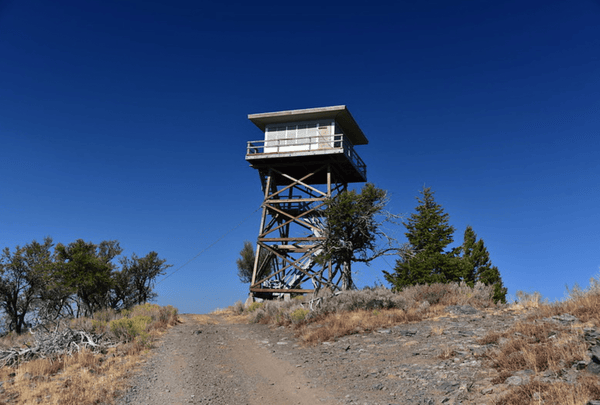 Remote fire lookout tower on a rocky trail surrounded by trees and blue sky during the Tahoe to Lassen Weekend Offroad adventure.