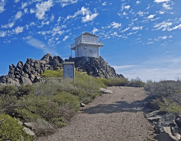 Historic fire lookout tower on rocky hilltop under a blue sky with scattered clouds along the Tahoe to Lassen adventure route.