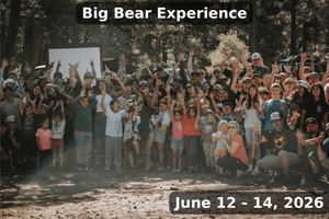 Large group photo of families, kids, and overland enthusiasts gathered in the forest during the Big Bear Experience hosted by Weekend Offroad from June 12–14, 2026, showing smiling participants raising their hands for a fun community moment.