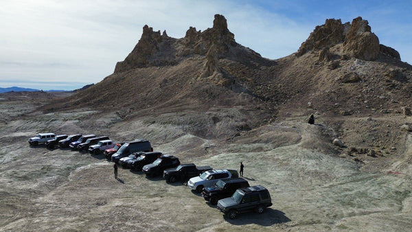 A lineup of off-road vehicles parked at the base of the Trona Pinnacles rock formations during the Valentines Overland Experience 2025 adventure.