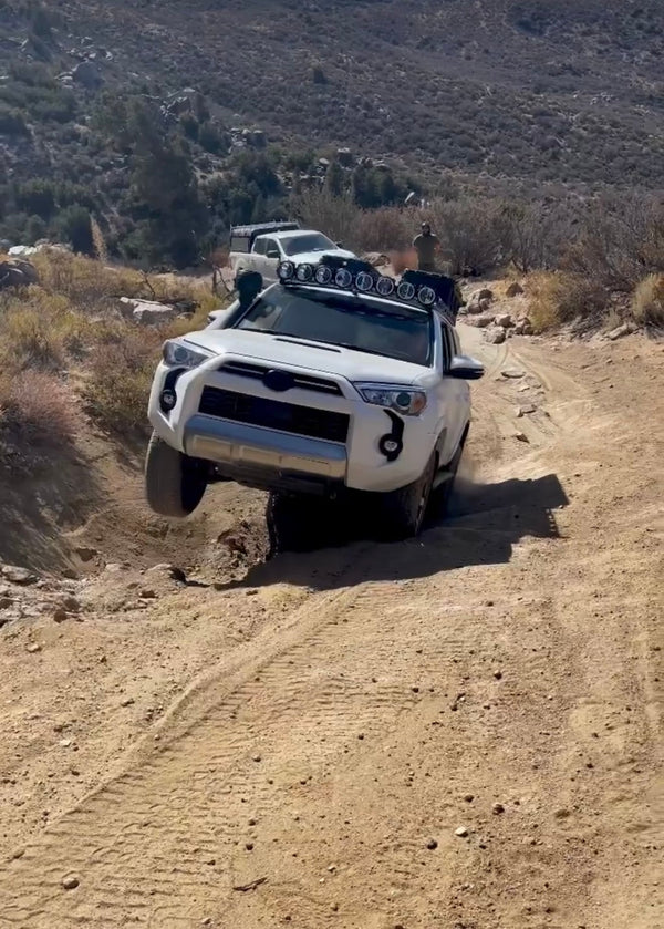 White Toyota 4Runner lifting a wheel while navigating uneven terrain during the Weekend Offroad Driving Workshop, demonstrating suspension articulation and technical driving skills.