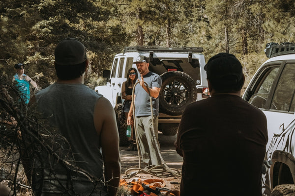 Instructor demonstrating proper off-road recovery rope techniques during the Trail Recovery & Emergency Skills Workshop, with participants watching and vehicles in the background.
