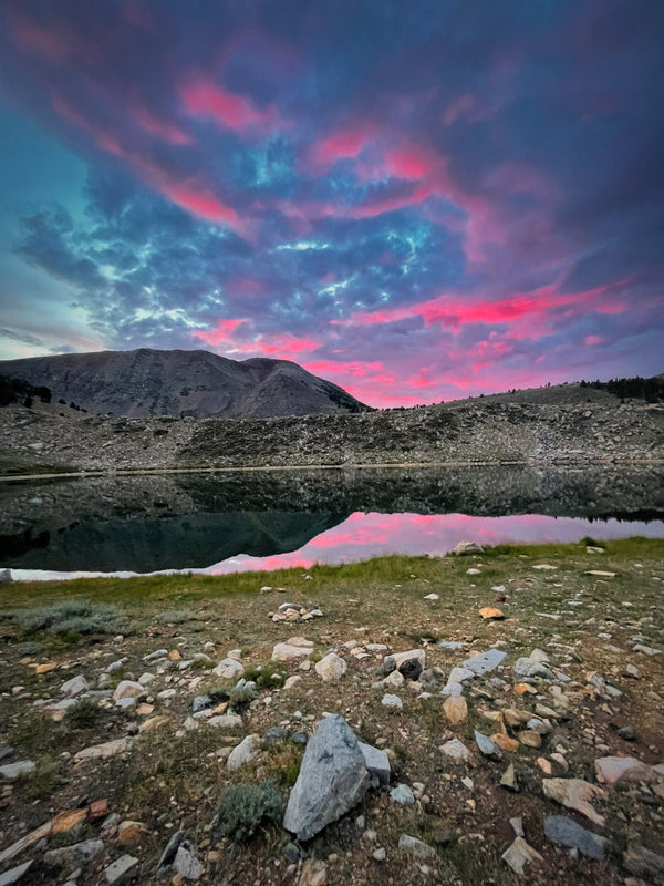 A vibrant pink and blue sunset reflects perfectly off a still alpine lake surrounded by rocky terrain during the Coyote Flats overland trip, September 4–7, 2026.