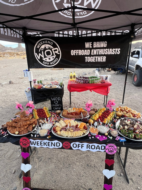 A beautifully decorated outdoor food setup with charcuterie boards, croissants, fruits, and drinks under a Weekend Offroad canopy during the Valentines Experience 2025 camping event.