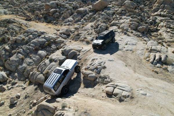 Two off-road vehicles practicing winch recovery during the Weekend Offroad Driving Workshop, with one truck assisting another on steep rocky terrain to teach safe recovery techniques.