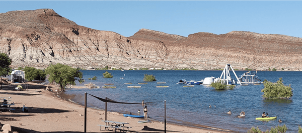 Lake and beach area with swimmers, kayaks, trees, and floating play structures during the Lake and Canyon Relaxation 2026 trip.