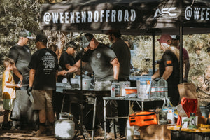 Volunteers serving food at a Weekend Offroad camping event, with families and kids waiting under the Weekend Offroad canopy.