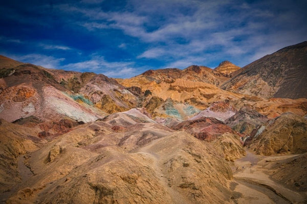 Colorful rock formations at Artist’s Palette in Death Valley with shades of pink, yellow, green, and purple under a partly cloudy blue sky.