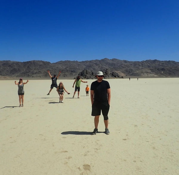 Group of people posing and jumping on the dry lakebed at Racetrack Playa in Death Valley with mountains in the background under a clear blue sky.