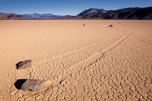 The Racetrack Playa in Death Valley featuring moving rocks and long trail marks across the cracked dry lakebed with mountains in the distance.