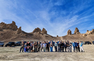 Large group of families and off-road enthusiasts standing together in front of desert rock formations during a Weekend Offroad adventure event.